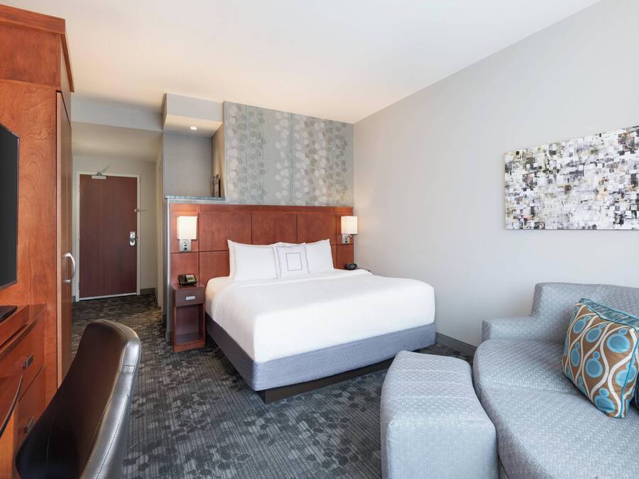 Ein Hotelzimmer mit Bett, Schreibtisch, Sessel, Sofa und einem an der Wand befestigten Fernseher.