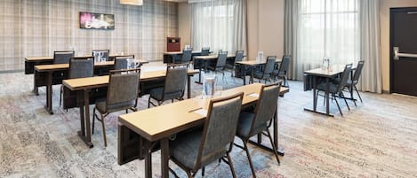A conference room with multiple tables and chairs, large windows with curtains, and a patterned carpet.