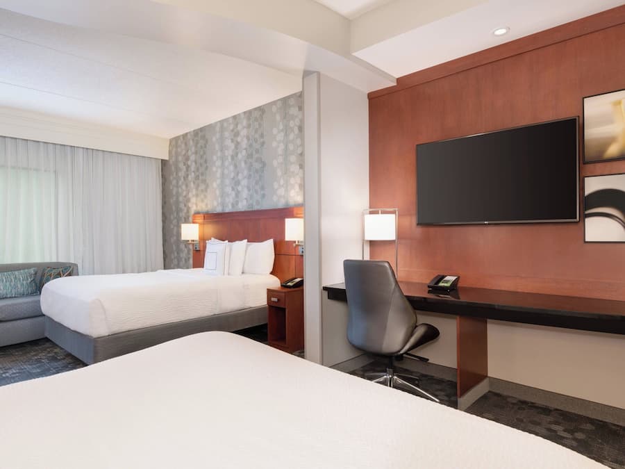 A hotel room with a bed, a desk, a chair, a TV, and a sofa.