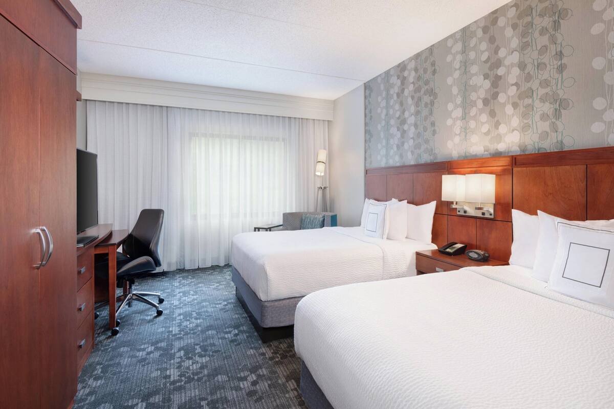 Une chambre d’hôtel avec deux lits, un bureau, une chaise et une armoire.