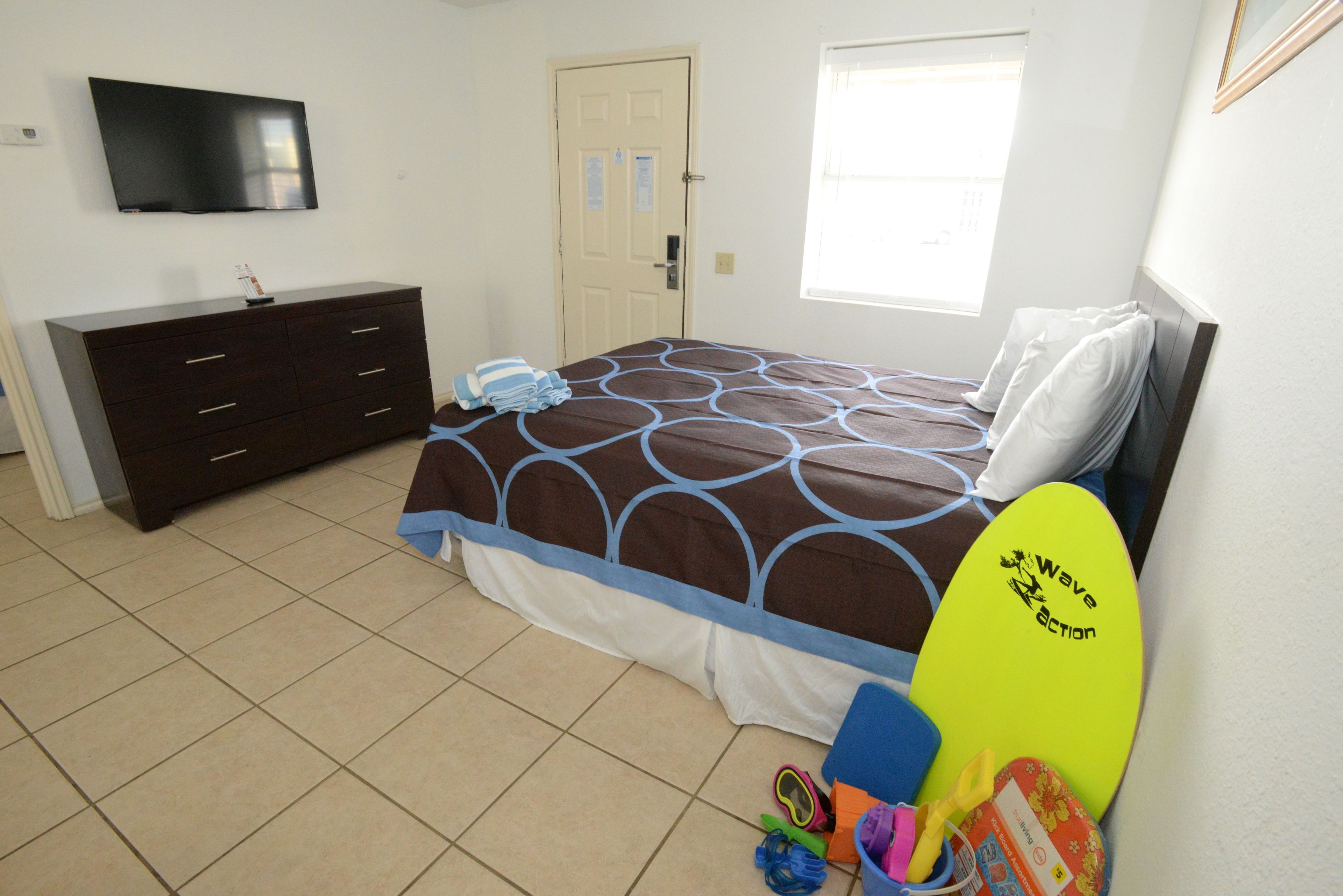 Un dormitorio con cama, cómoda, televisor y ventana.