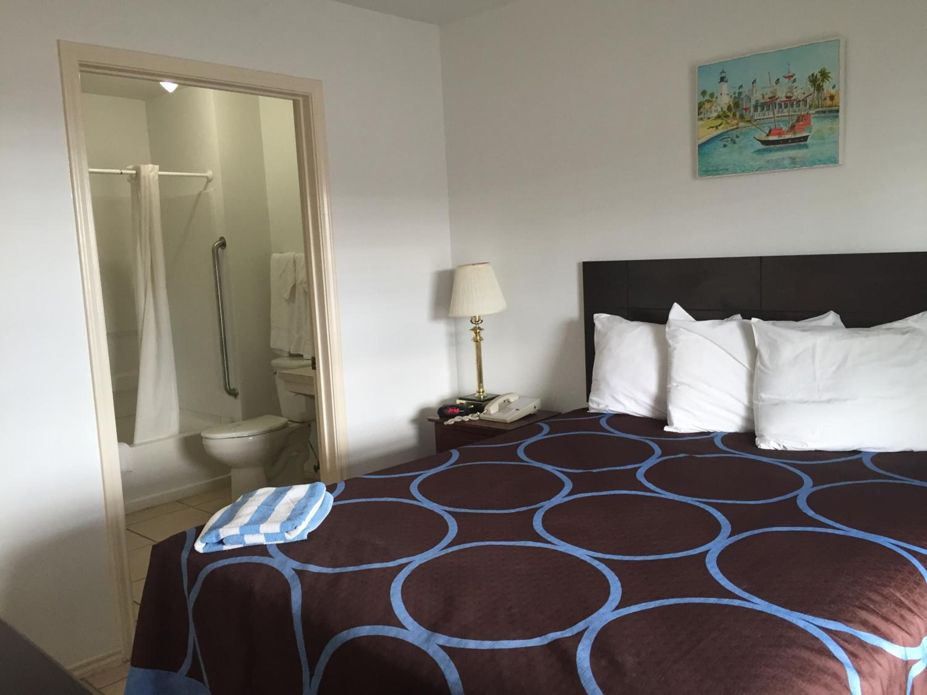 Ein Hotelzimmer mit Bett, Dusche, Toilette und einem Bild mit einer Strandansicht.