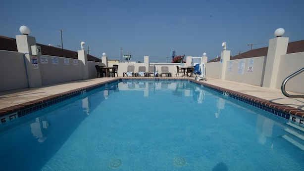 A swimming pool with a clear blue water, surrounded by lounge chairs and a white wall with signage.