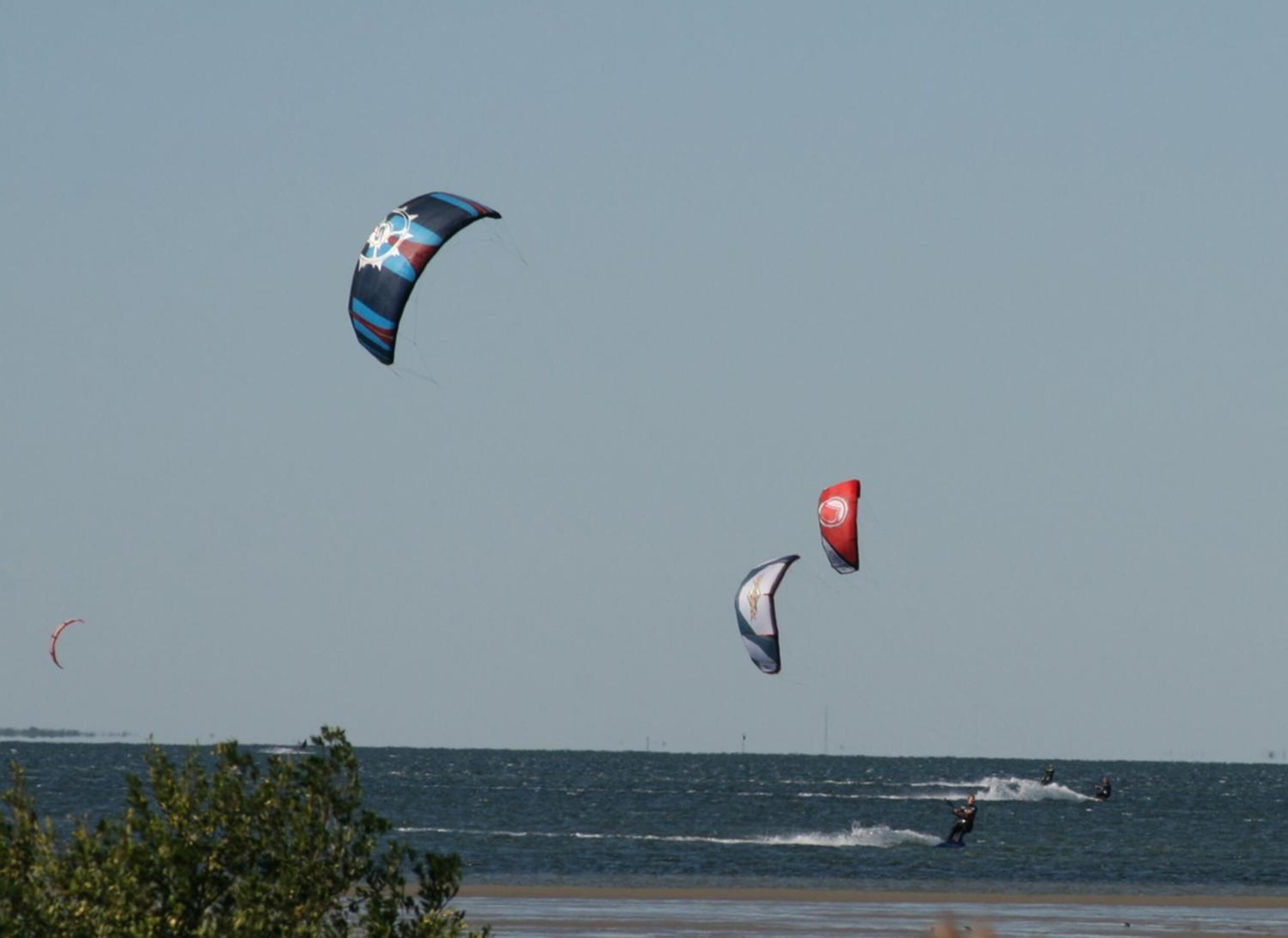 Una playa con gente practicando windsurf y kitesurf.