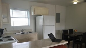 A kitchen with a stove, sink, refrigerator, and a laptop on the counter.