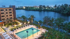 A swimming pool with lounge chairs and umbrellas, surrounded by greenery and overlooking a body of water.