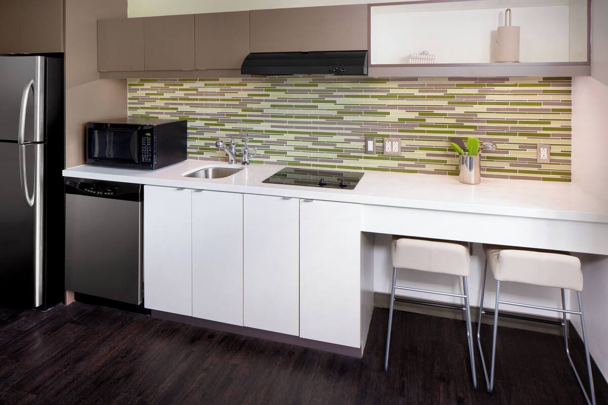 A modern kitchen with a stainless steel refrigerator, a black microwave, a double sink, and two bar stools.