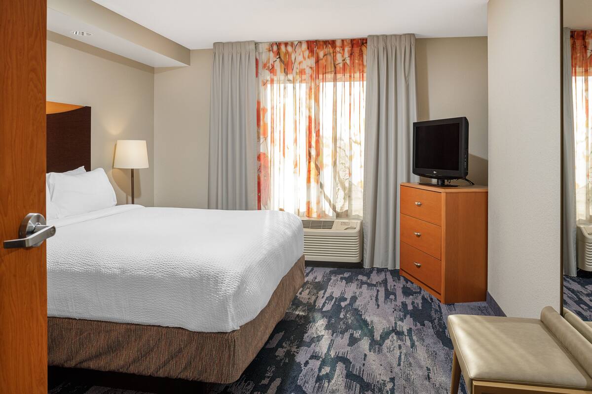 A hotel room with a bed, a television, a dresser, and a window with curtains.