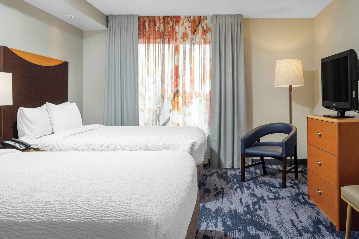A hotel room with two beds, a desk, a chair, a TV, and a window with curtains.