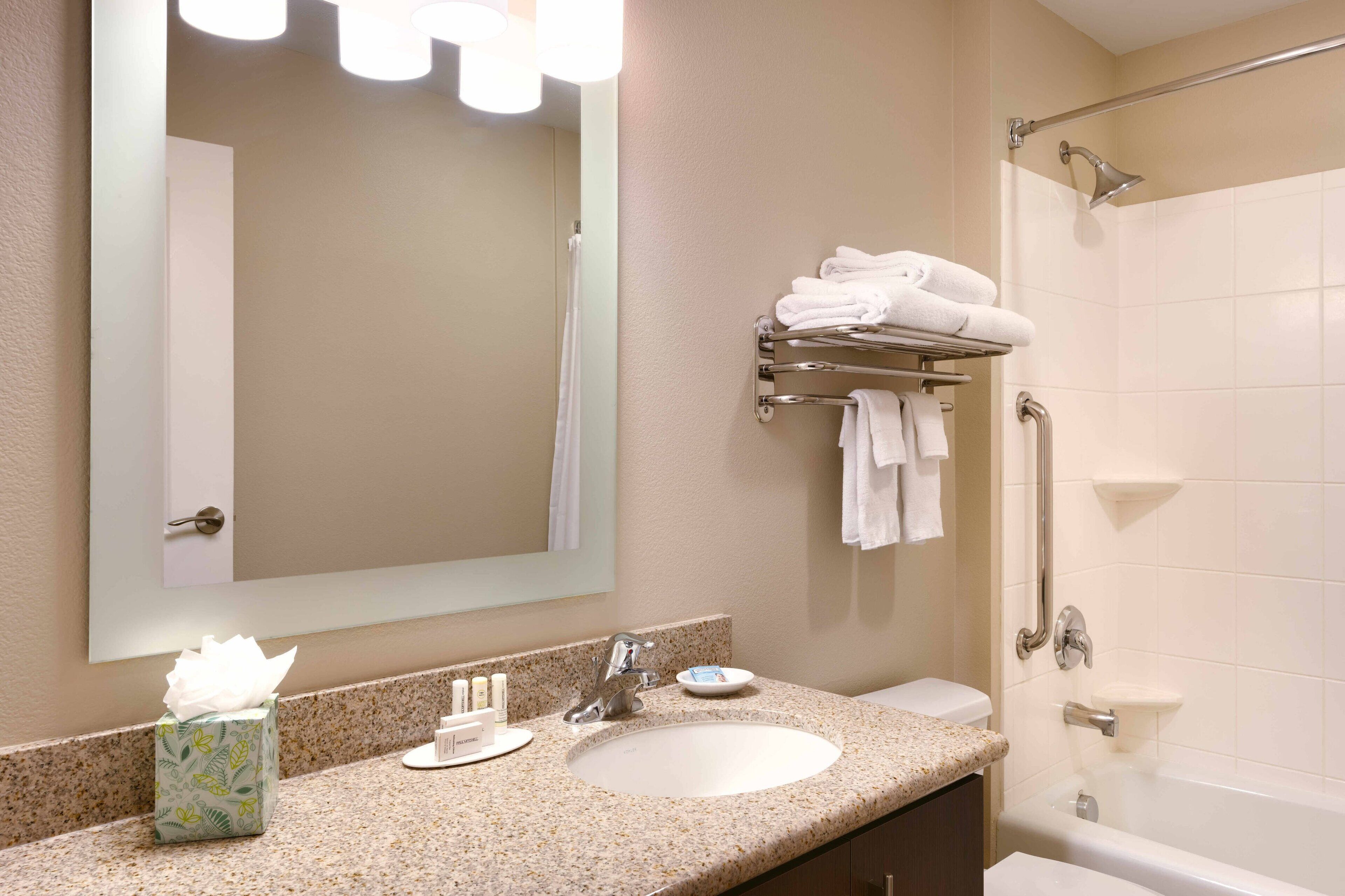 A bathroom with a sink, mirror, towel rack, and a shower area.
