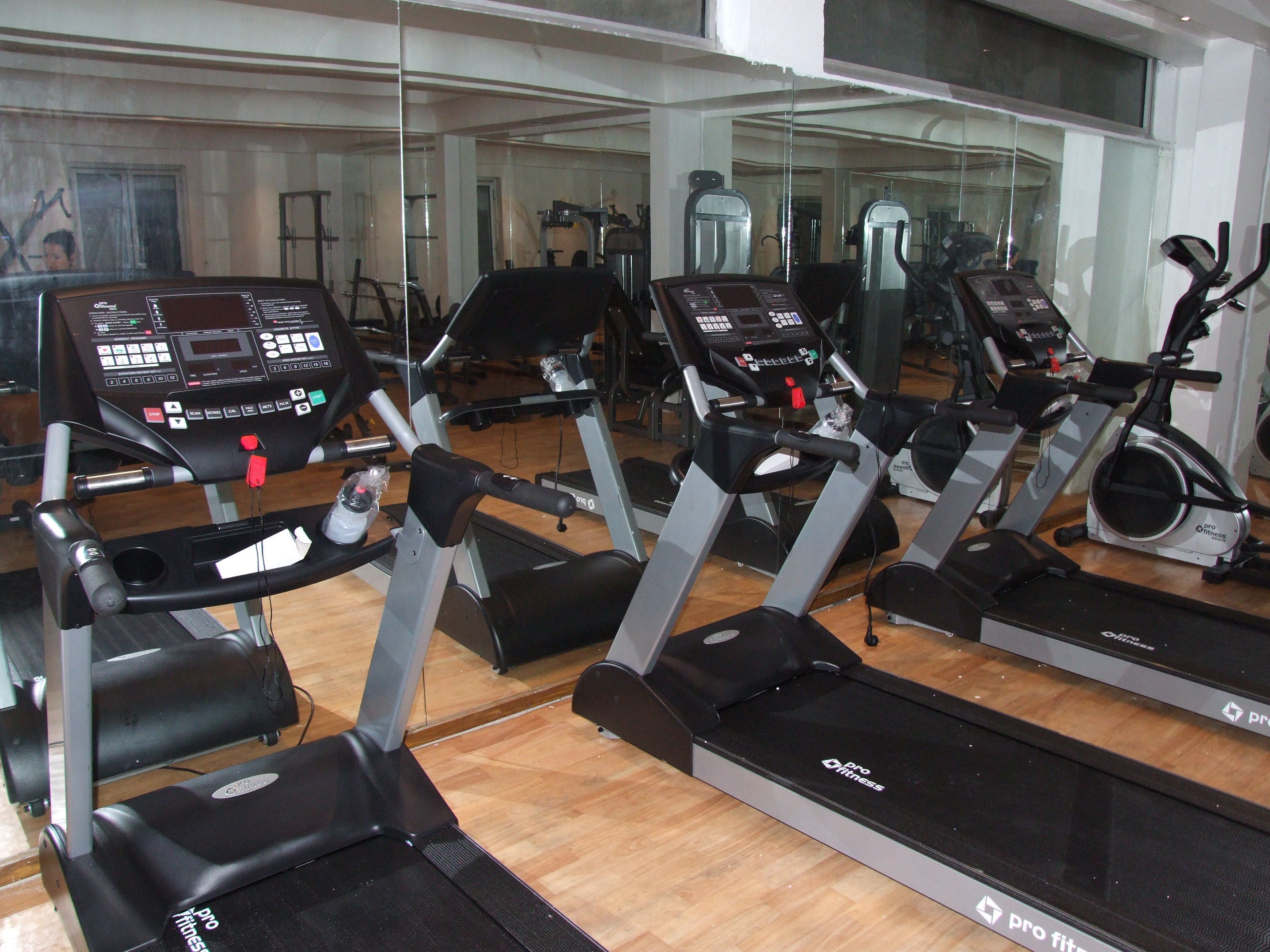 Academia com várias esteiras de corrida Pro Fitness, espelhos e equipamentos de ginástica.