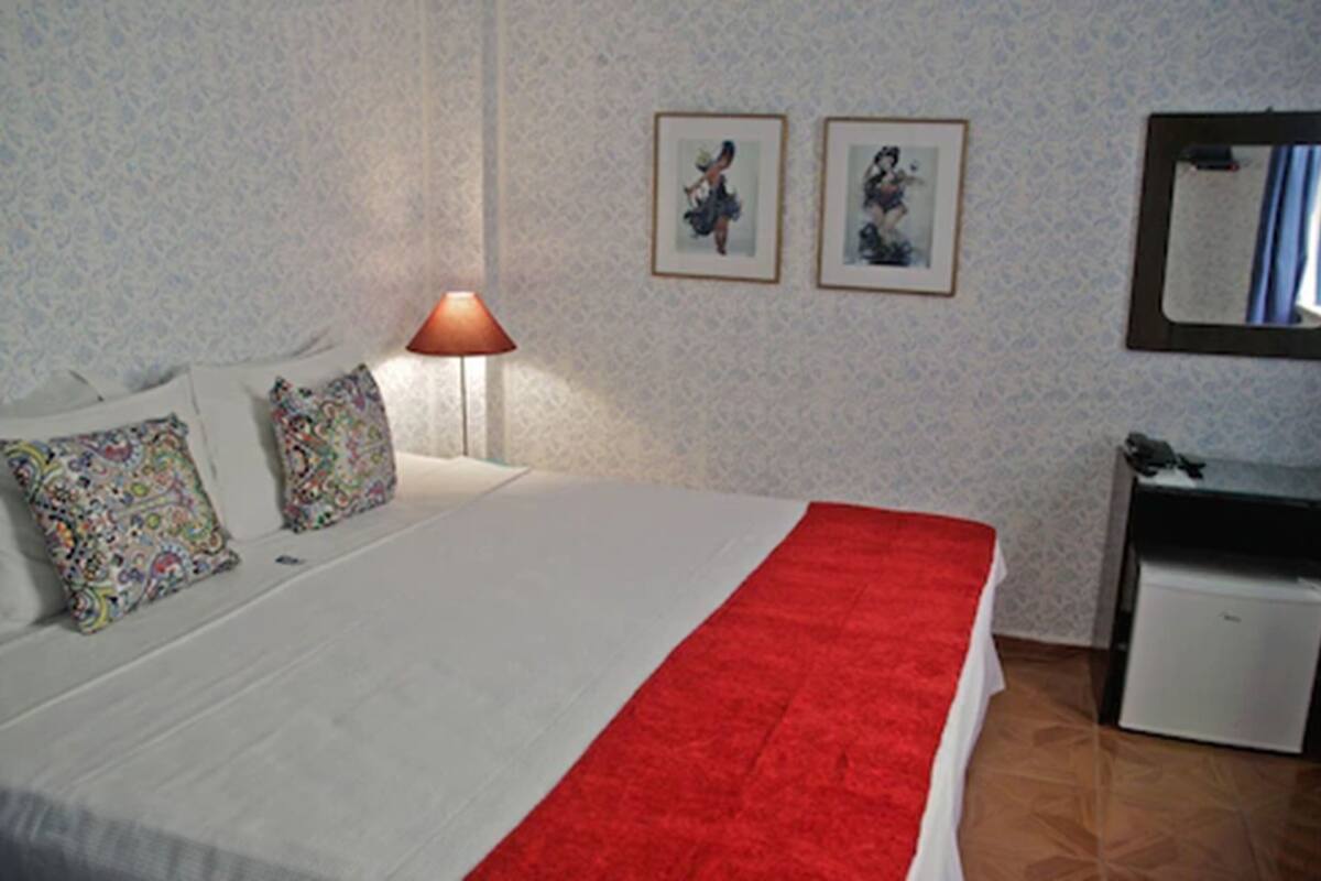 Habitació d'hotel amb llit, escriptori, làmpada i dos quadres penjats a la paret.