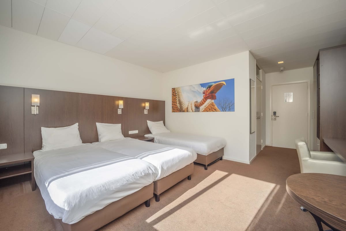 Une chambre d’hôtel avec deux lits, un téléviseur à écran plat, un tableau au mur et une porte donnant sur une autre pièce.