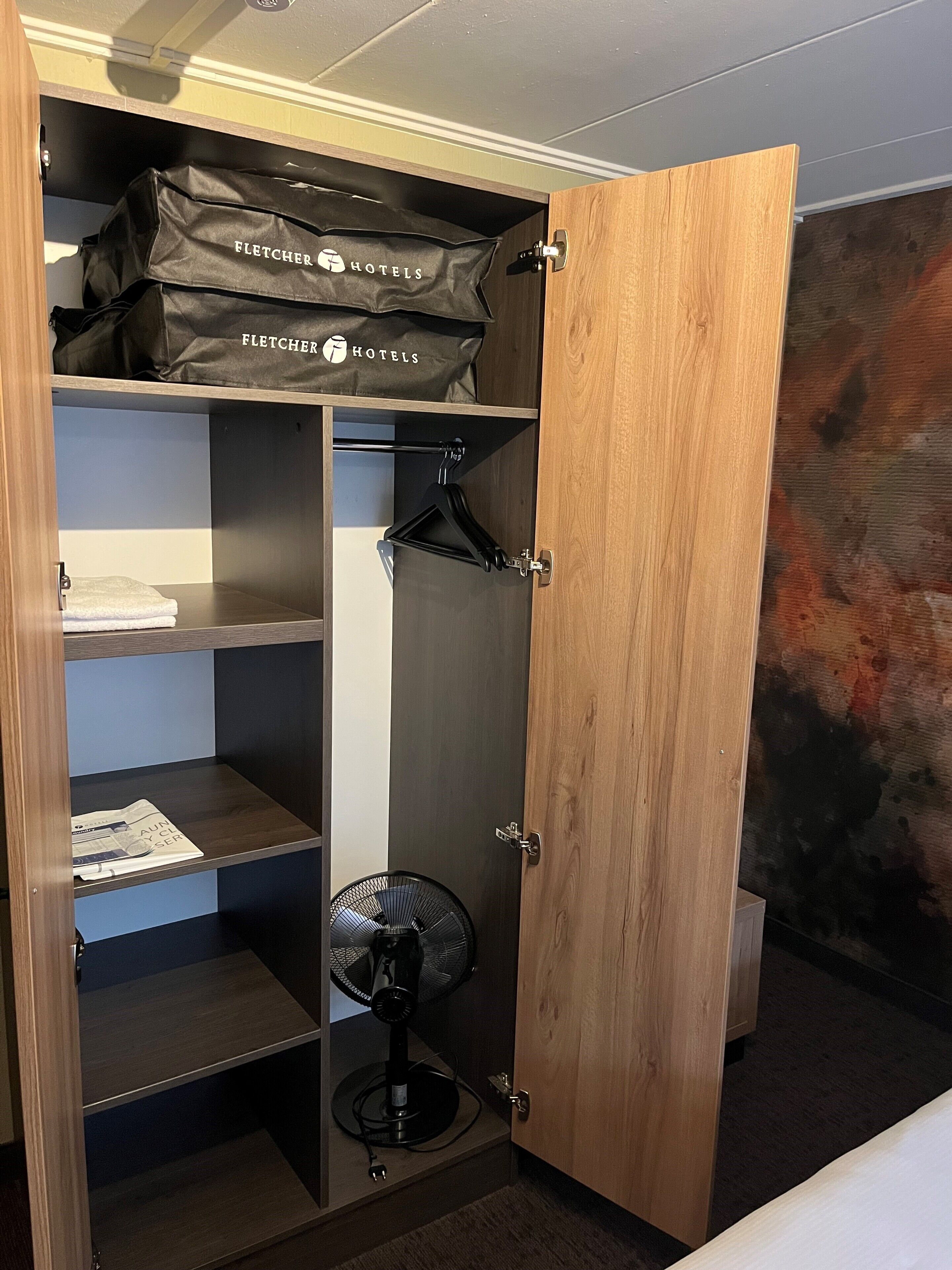 Une chambre d’hôtel avec un placard contenant des cintres, un ventilateur et une serviette pliée.