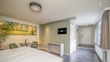 Ein Hotelzimmer mit einem großen Bett, einem Schreibtisch, einem Sessel, einem Fernseher und einem Landschaftsbild.