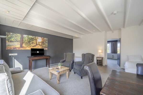 A hotel room with a large TV, striped armchairs, a wooden coffee table, and a view of the outdoors. - Fletcher Hotel - Restaurant Waalwijk (Waalwijk)