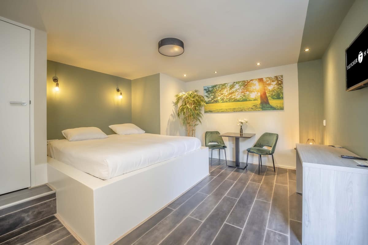 Une chambre moderne avec un grand lit, un bureau, deux chaises, une petite table et un téléviseur fixé au mur.