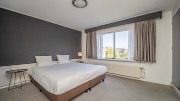 Une chambre d’hôtel avec un grand lit, une petite table, une fenêtre avec des rideaux et un radiateur.