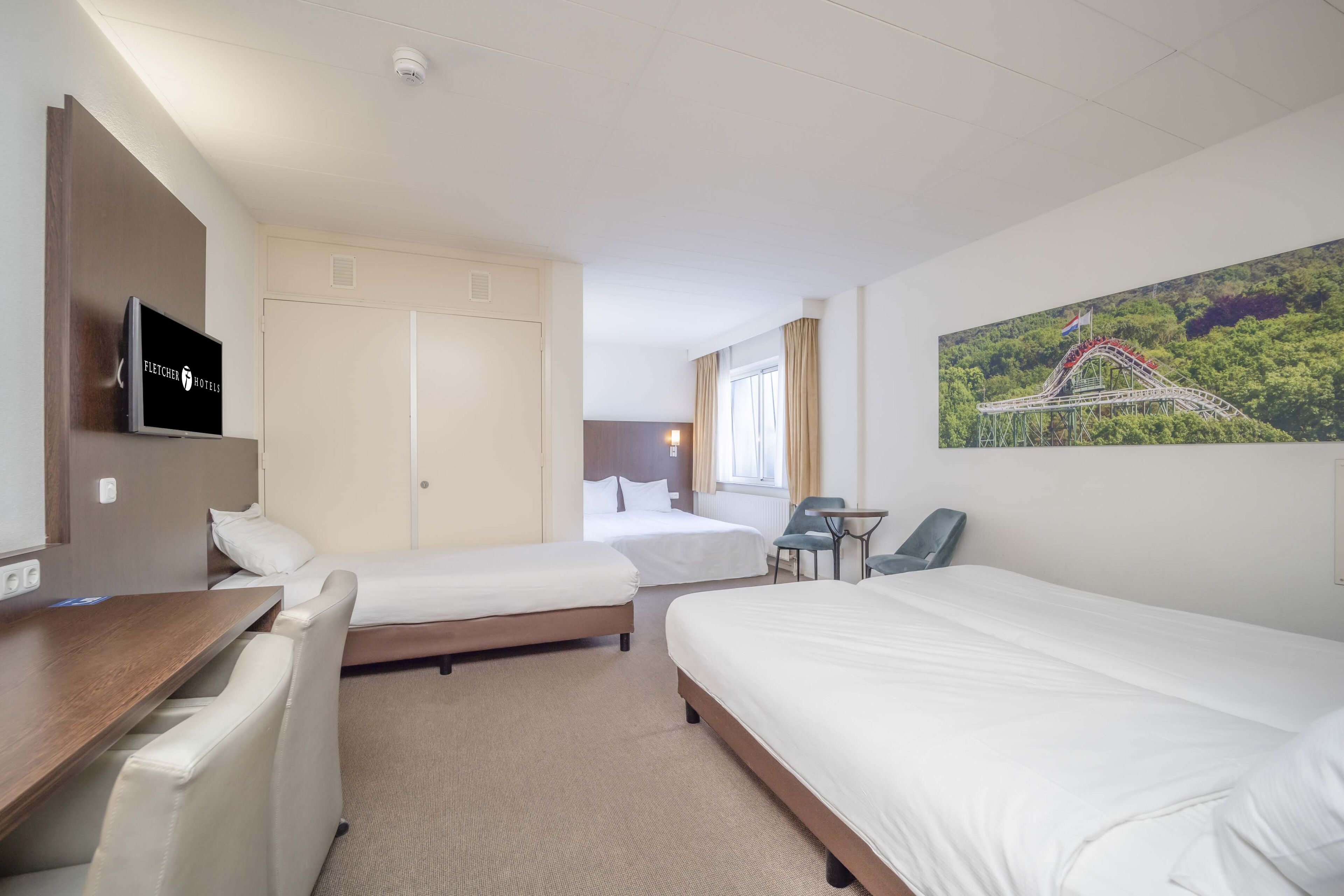 A hotel room with two beds, a desk, a chair, a TV, a window with curtains, and a painting of a roller coaster.
