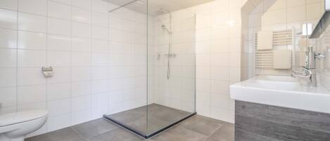 A modern bathroom with a glass-enclosed shower, a white toilet, and a vanity with a mirror.