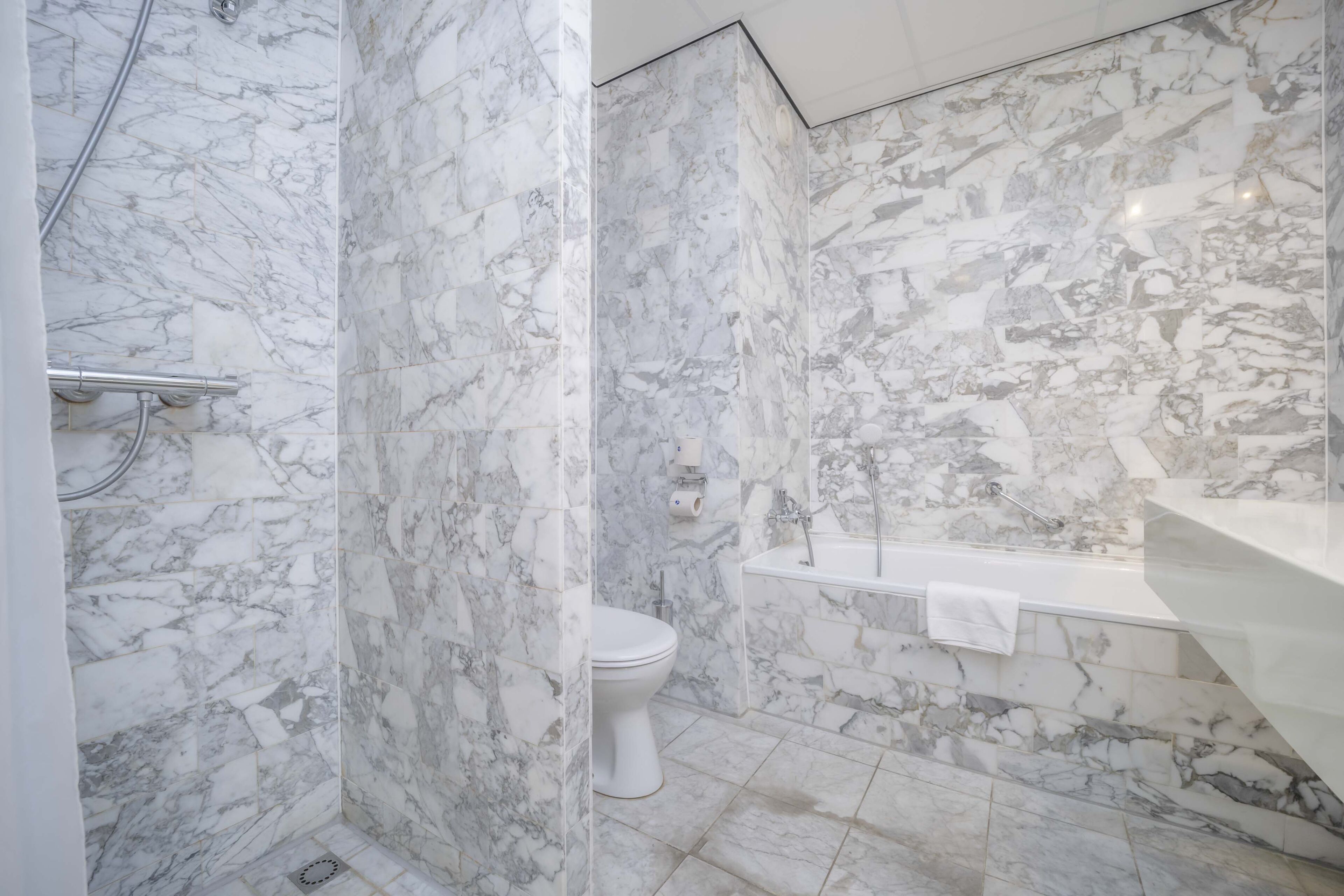 A bathroom with marble walls, a toilet, a bathtub, and a shower area.