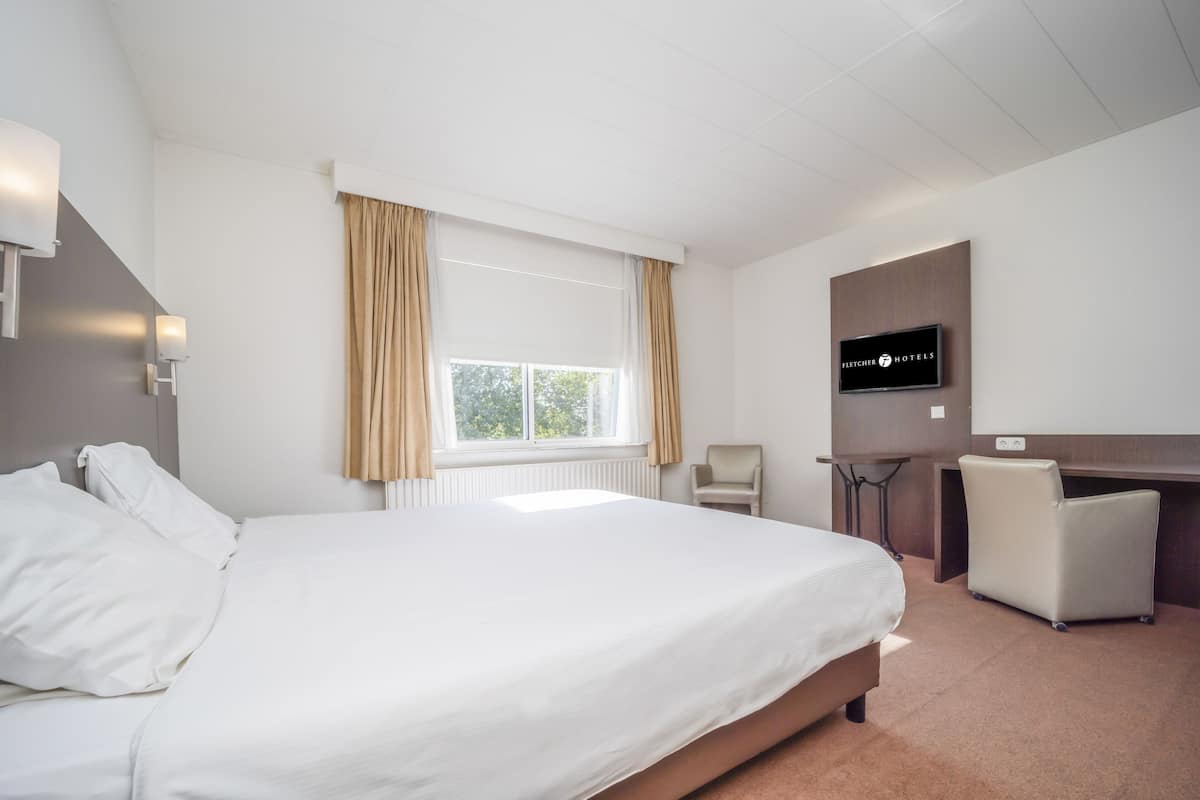 Une chambre d’hôtel avec un grand lit, un bureau, une chaise et un téléviseur.