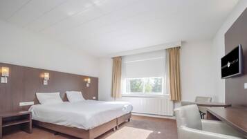 A hotel room with a bed, bedside tables, a desk, a chair, and a TV.