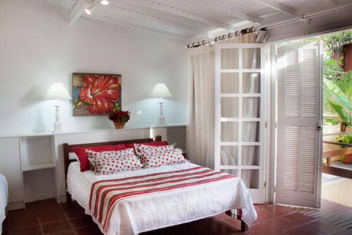 A bedroom with a bed, two bedside tables with lamps, a painting, and a sliding glass door leading to an outdoor area.