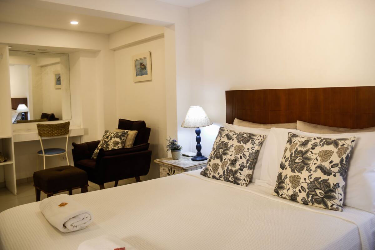 A hotel room with a bed, a desk, a chair, a lamp, and a mirror.