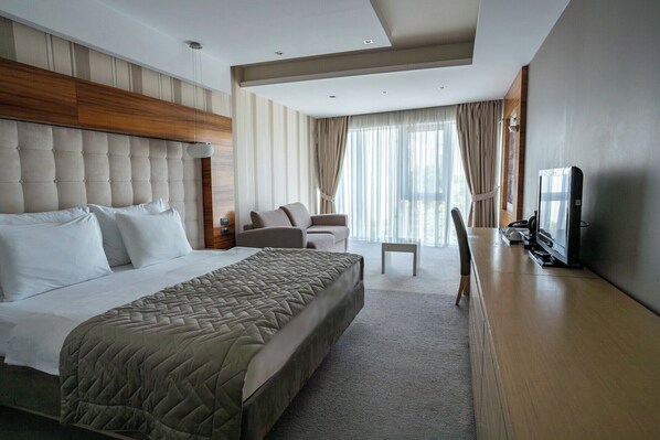 A modern hotel room with a large bed, a sofa, a TV, and a desk. - Garni Hotel Centar (Novi Sad)