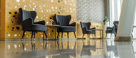 A modern lobby with a reflective floor, a patterned wall, and a seating area with dark chairs and a small table.