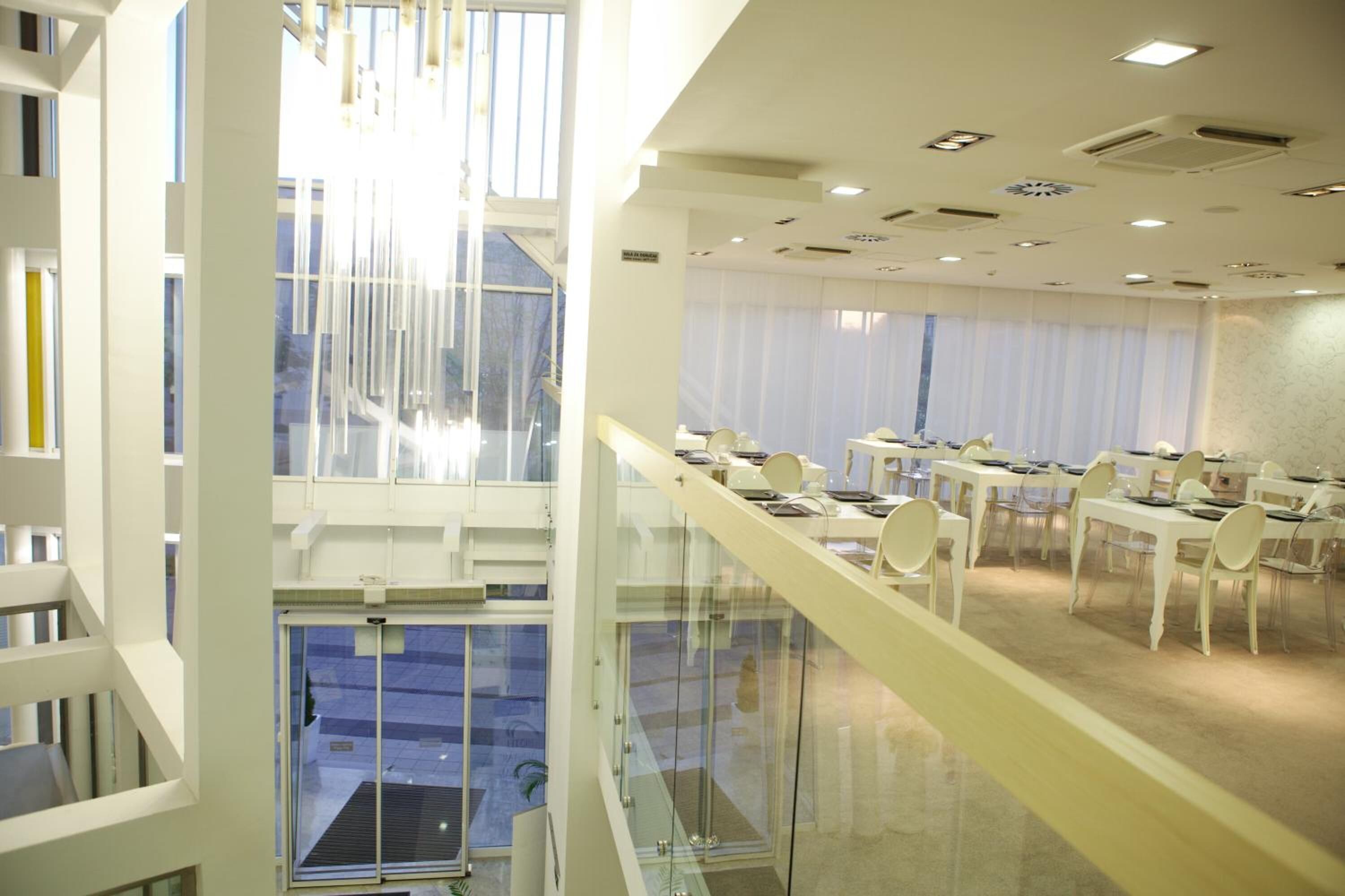 Een moderne hotellobby met een glazen trap, meerdere eettafels en stoelen.