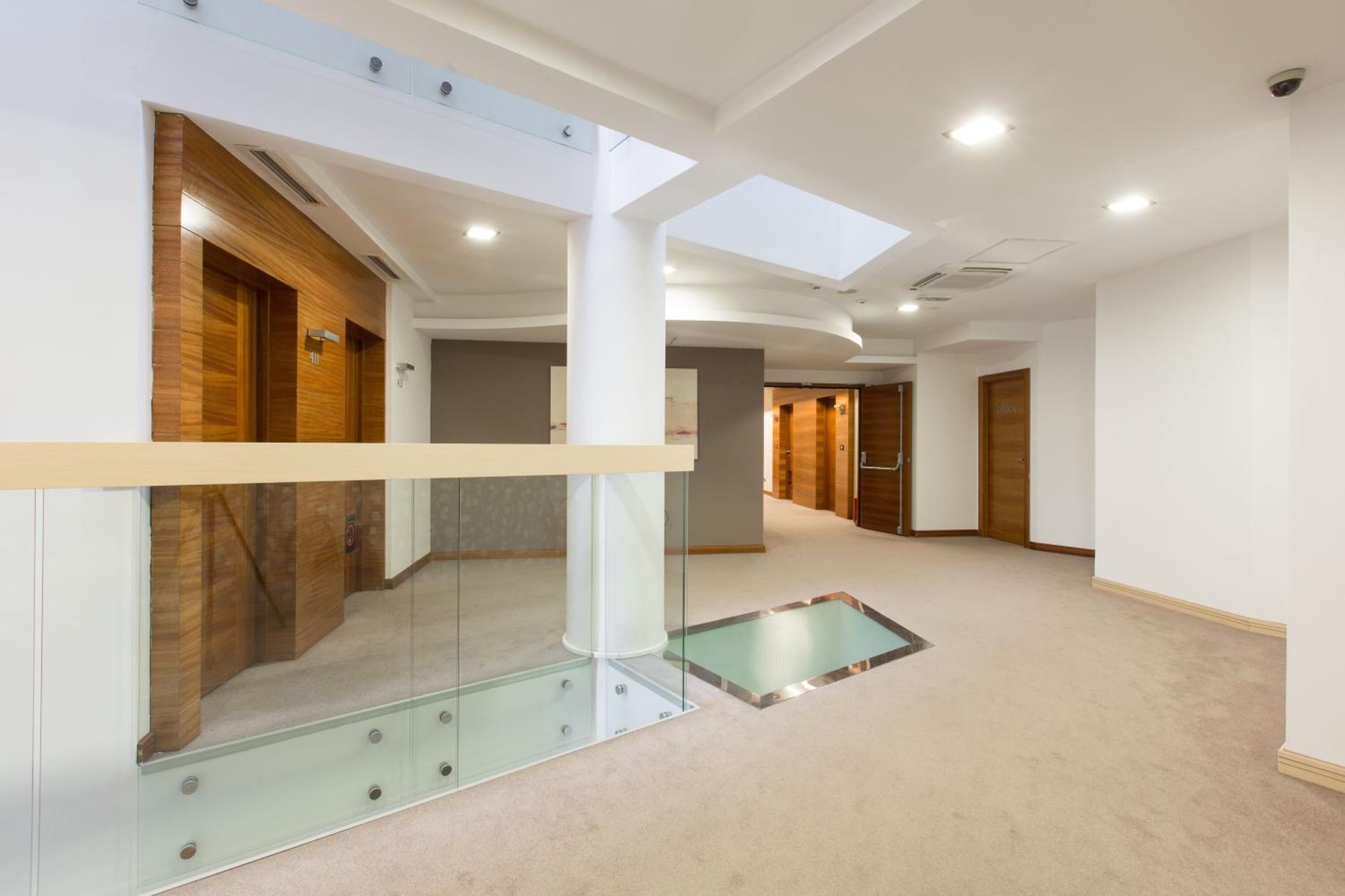 A modern hotel interior with a glass partition, a central light fixture, and a carpeted floor.