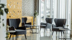 A modern lobby with two black armchairs, a small table, and a potted plant. - Garni Hotel Centar (Novi Sad)