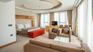 A hotel room with a bed, a TV, a sofa, and a coffee table. - Garni Hotel Centar (Novi Sad)