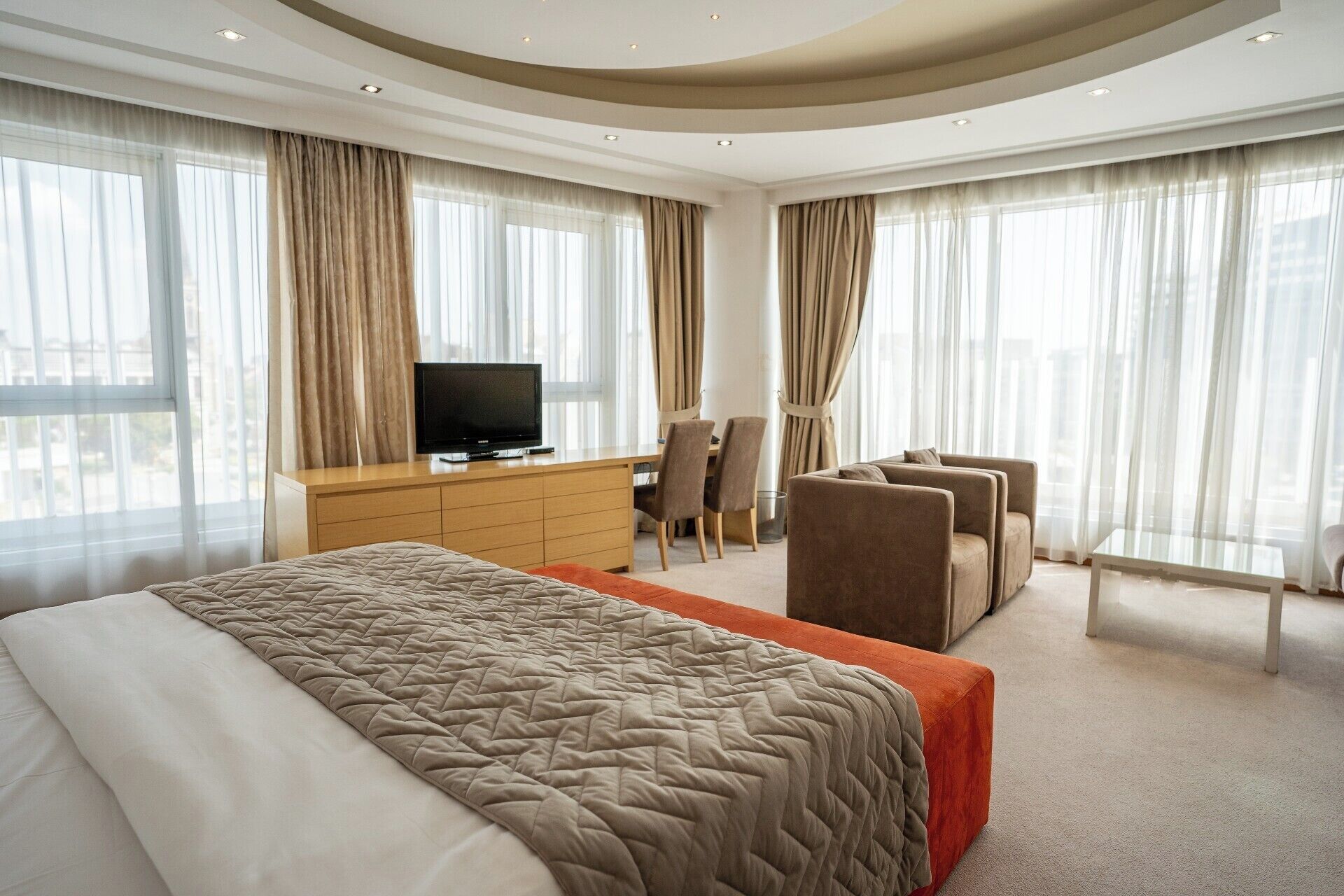 Una habitación de hotel moderna con una cama grande, un escritorio con televisor y una zona de estar.