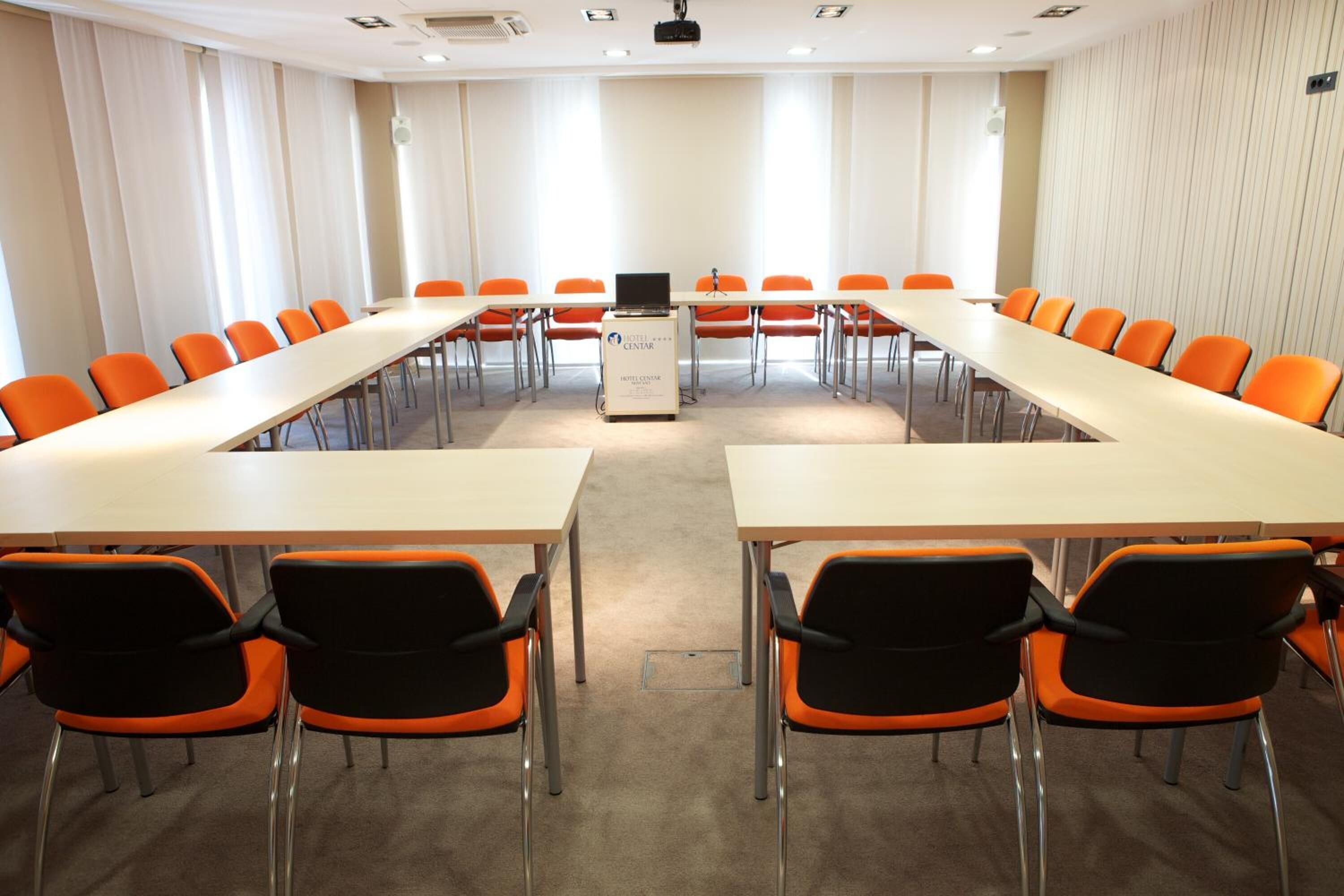 A conference room with a long table, orange chairs, and a podium.