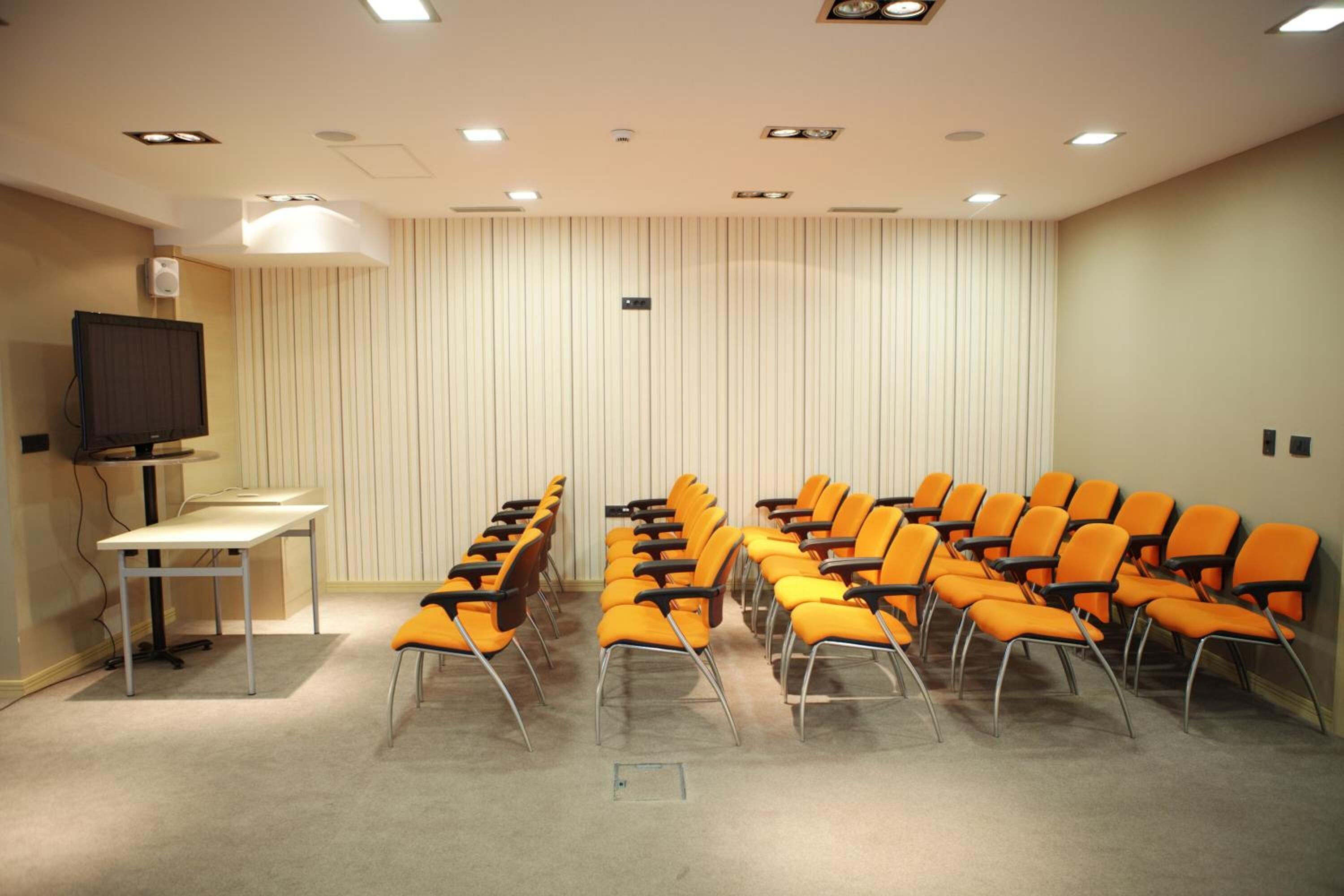 A conference room with rows of orange chairs, a white table, and a television on the left.