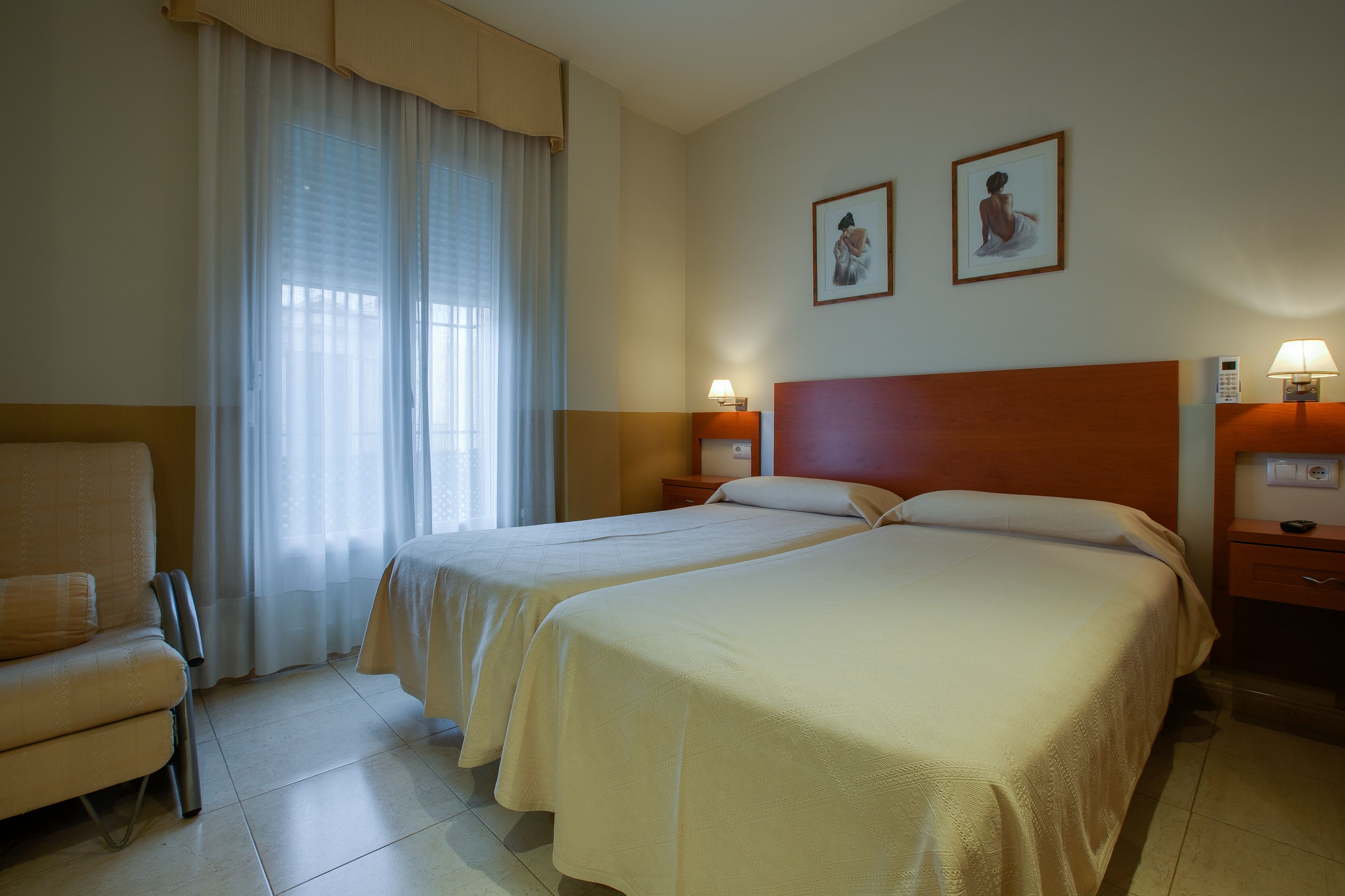 Una habitación de hotel con dos camas, una silla, un escritorio y una ventana con cortinas.