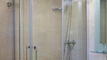 Un box de ducha con paredes de vidrio, un cabezal de ducha manual, un lavamanos blanco con espejo arriba y un inodoro a la izquierda.