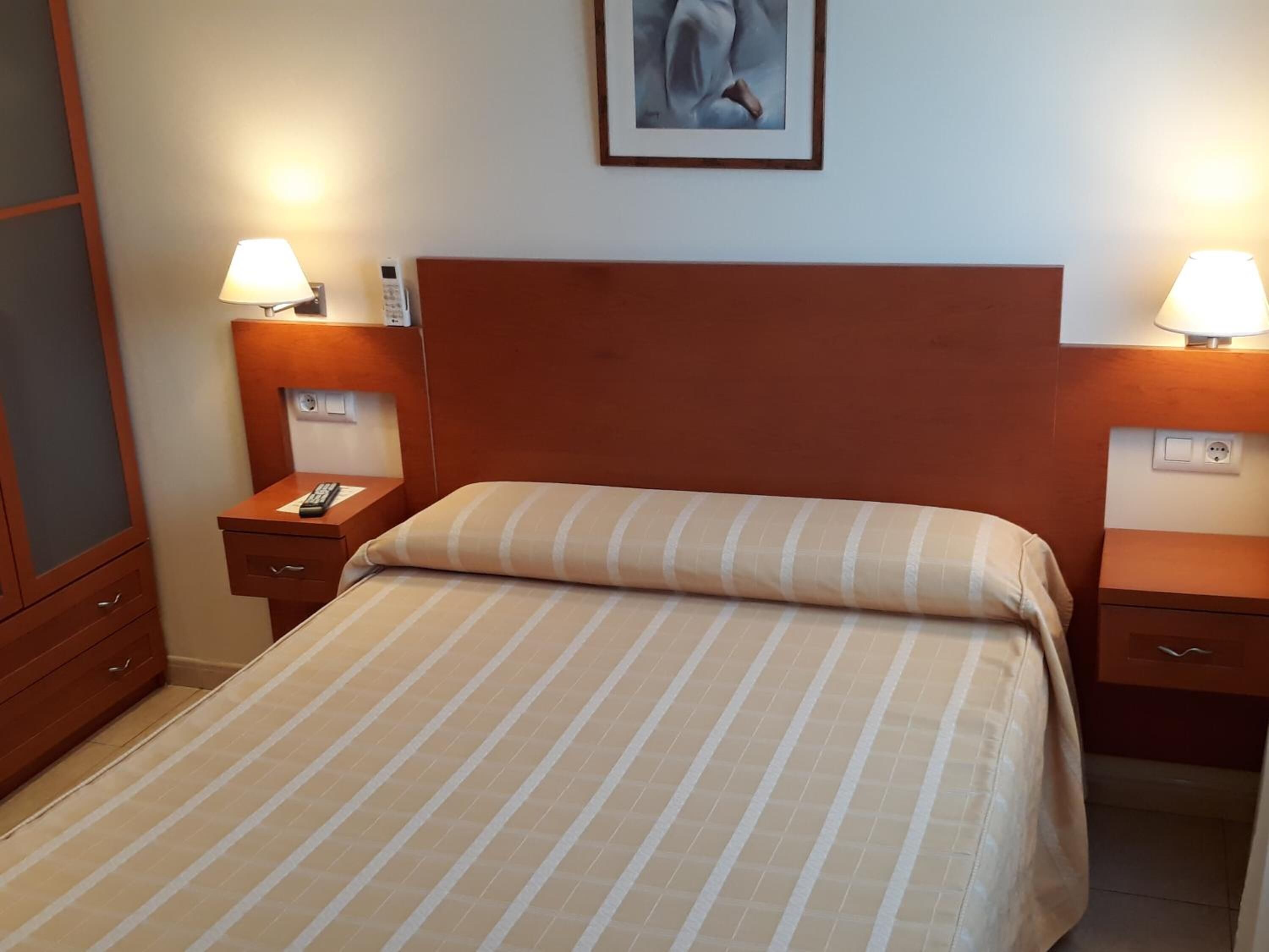 Een hotelkamer met een bed, twee nachtkastjes, een lamp en een schilderij aan de muur.