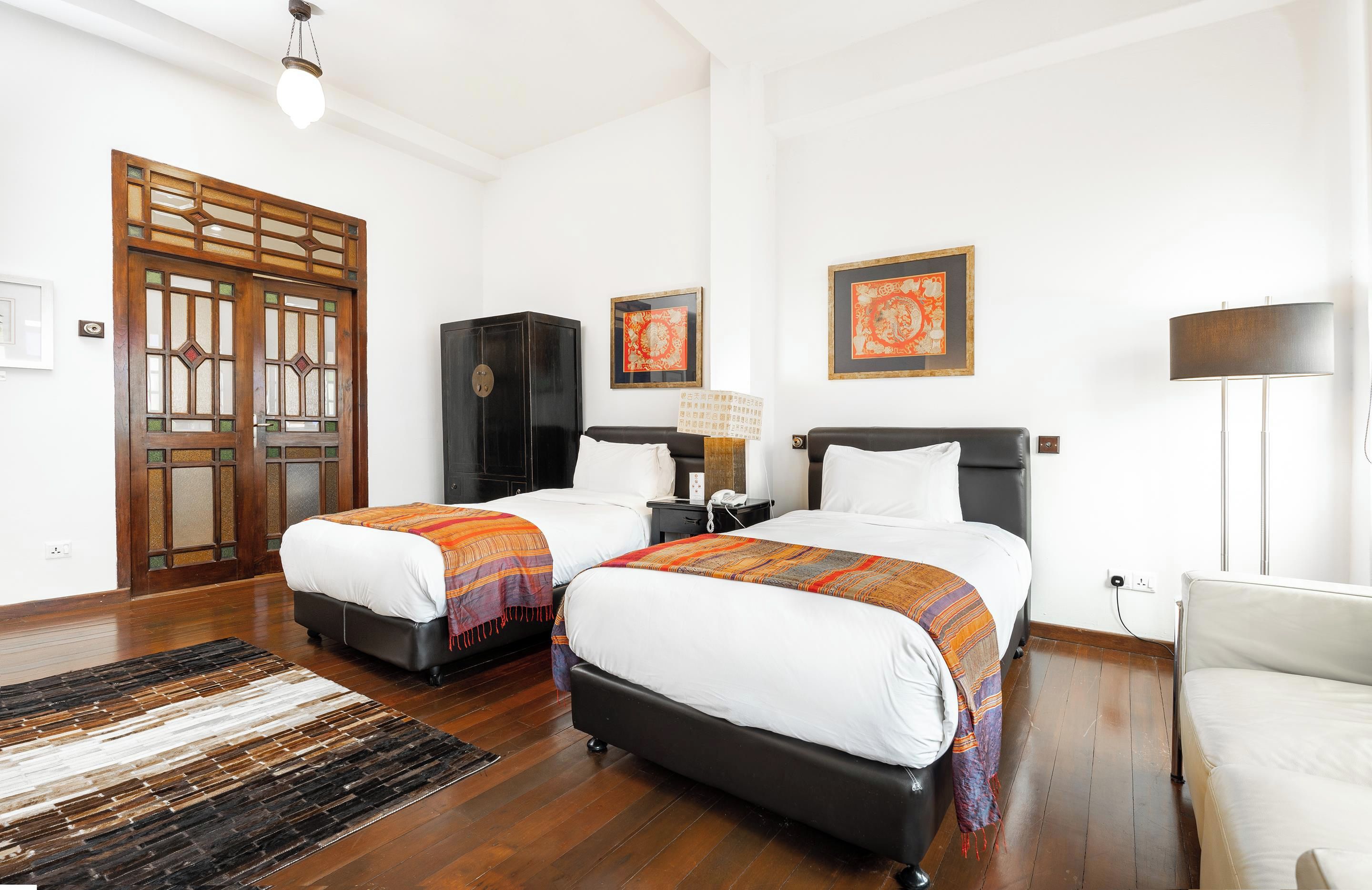 Habitación de hotel con dos camas, un armario, un escritorio, una silla y una lámpara.