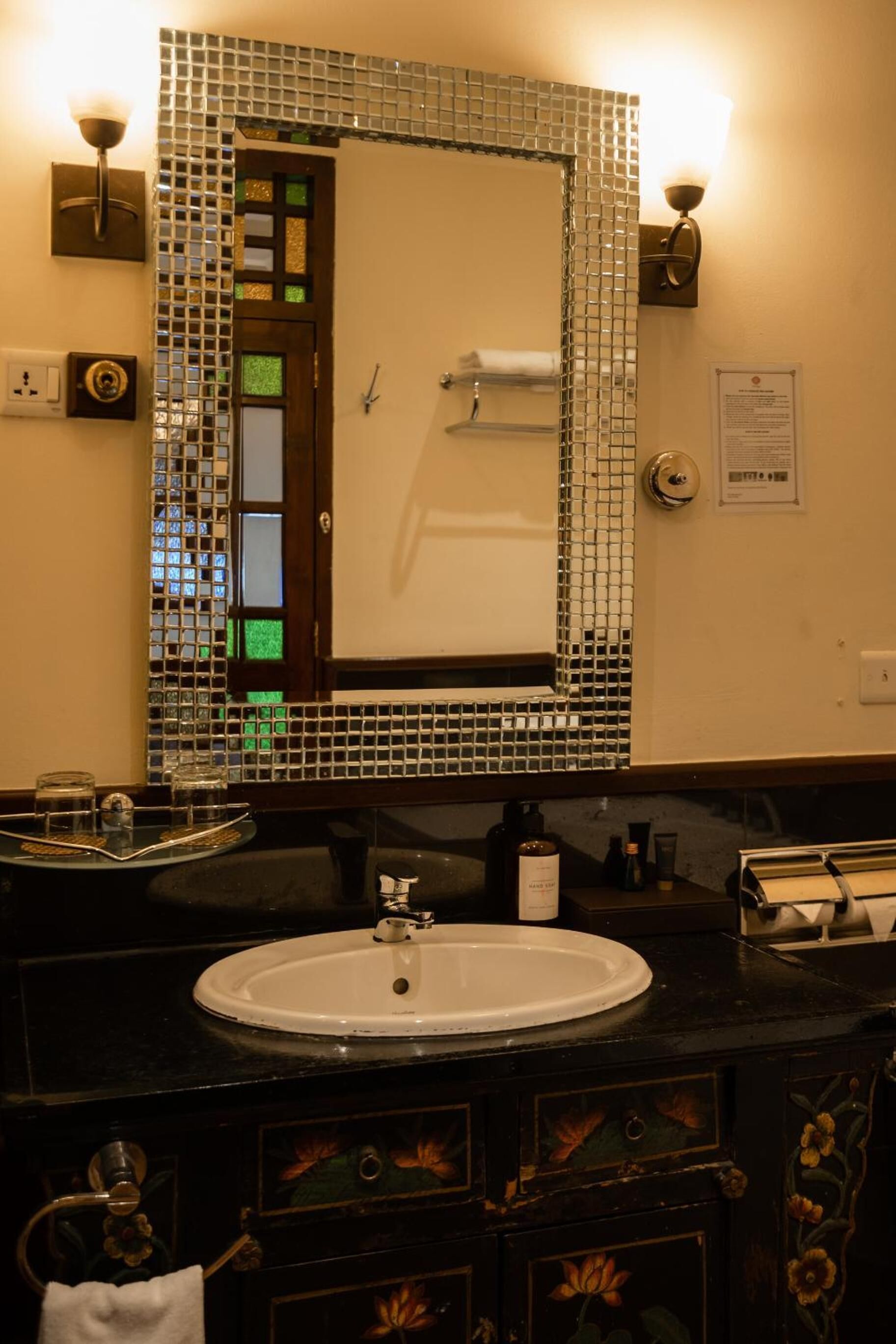 A bathroom with a round sink, a mirror with mosaic tiles, and a towel rack.