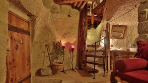 A rustic room with a wooden door, a stone wall, a wooden staircase, a wooden bench, and a red chair. - Koza Cave Hotel (Nevsehir)