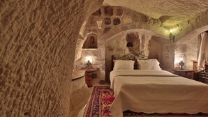 Una habitación acogedora y rústica con una pared de piedra, una cama con ropa de cama blanca, una alfombra estampada y dos lámparas de noche.