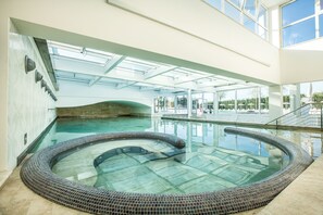 Ein großes Hallenbad mit Whirlpool, umgeben von einer gläsernen Galerie mit Blick ins Freie.