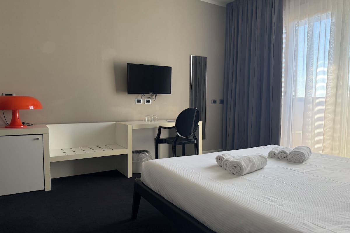 Ein Hotelzimmer mit einem Bett, einem Schreibtisch, einem Sessel, einem Fernseher und einem fenster mit Vorhängen.