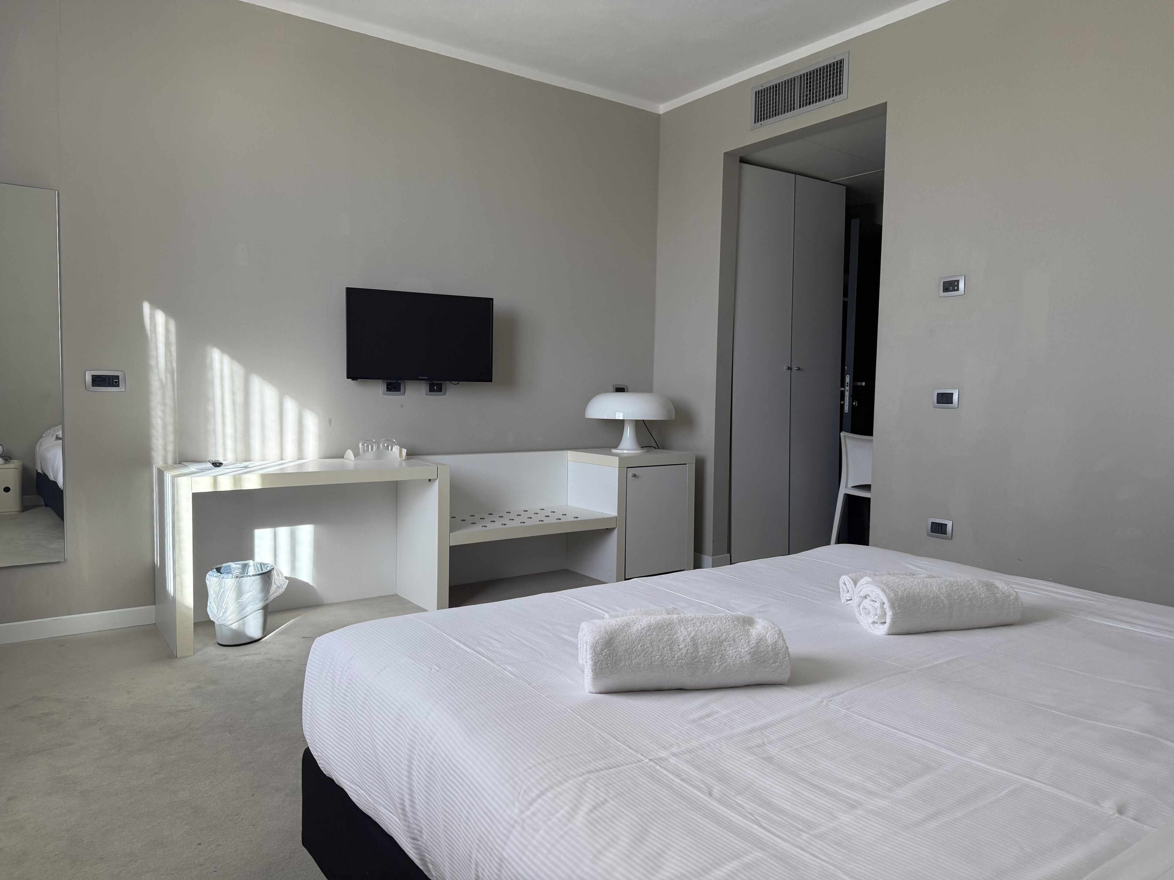 Una camera d'albergo con un letto, una scrivania, una sedia, una televisione e uno specchio.