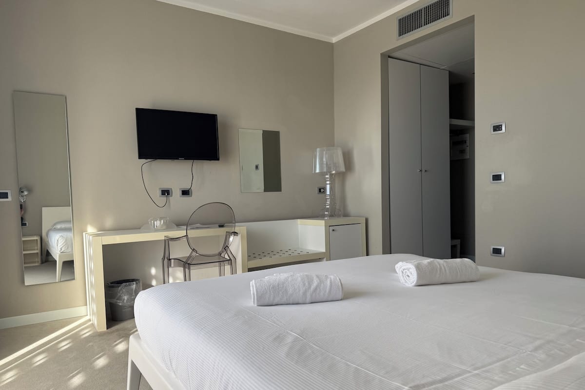 Ein Hotelzimmer mit einem großen Bett, einem Schreibtisch mit Stuhl, einem Fernseher und einem Kleiderschrank.