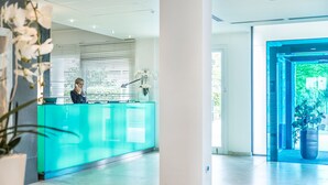Un espace d’accueil avec un comptoir en verre, une réceptionniste et une orchidée en pot.